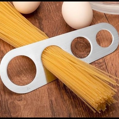 Suporte metálico de medição para esparguete com massa e ovos numa superfície de madeira