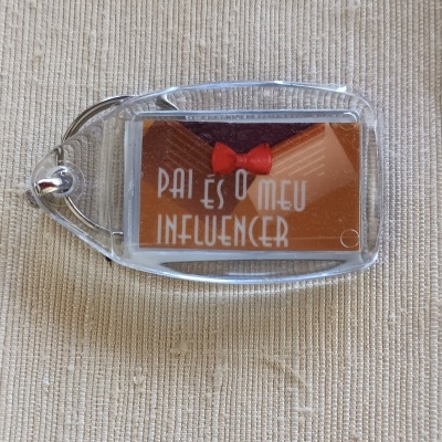 Chaveiro transparente com etiqueta castanha e vermelha com texto branco sobre tecido bege