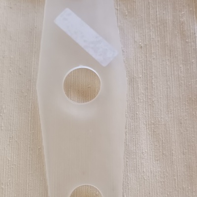 Peça plástica transparente com três orifícios circulares e etiqueta branca