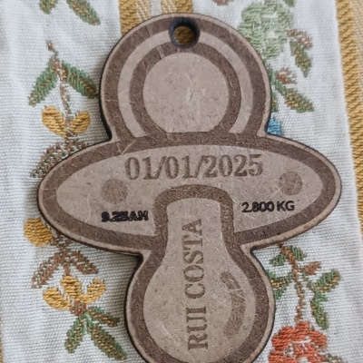 Etiqueta de papel em forma de chupeta com texto e padrão floral bordado em tecido