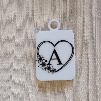 Chaveiro branco com coração, letra A e flores, sobre tecido bege