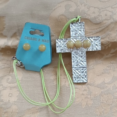 Conjunto de colar com cruz prateada texturizada e brincos amarelos no cartão azul