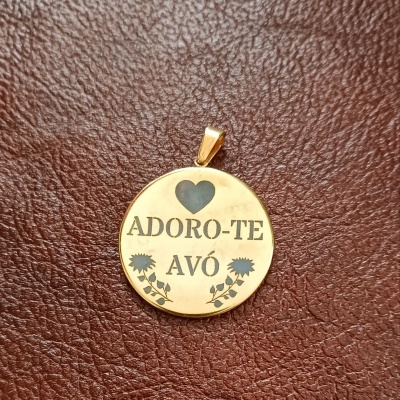 Medalhão dourado redondo com gravação preta e flores sobre fundo de couro castanho