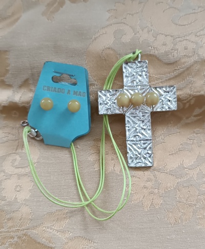 Conjunto de colar com cruz prateada texturizada e brincos amarelos no cartão azul