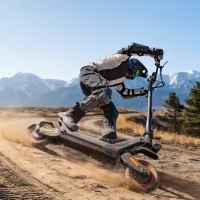 Pessoa em trotiente elétrica off-road preta com capacete e proteções em terreno de terra e montanhas ao fundo