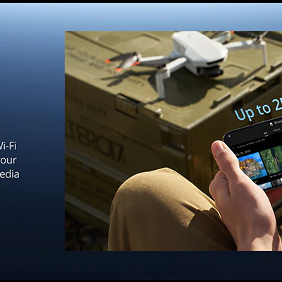 Pessoa a usar smartphone perto de drone branco sobre caixa verde ao ar livre