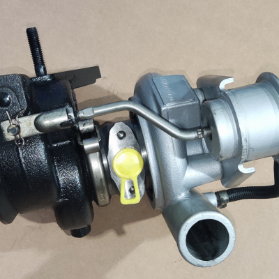 Turbolocompressor metálico com partes cinza, preto e amarelo sobre superfície bege