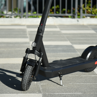 Scooter elétrico preto com roda dianteira e suspensão num chão de ladrilhos cinzentos