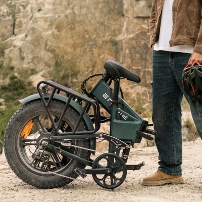 Bicicleta elétrica dobrável verde escura com pneus grossos e pessoa ao lado segurando capacete