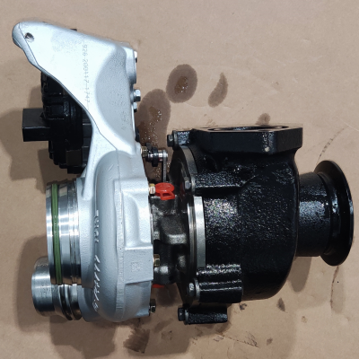 Peça mecânica de turbo prata e preta com manchas de óleo numa superfície castanha