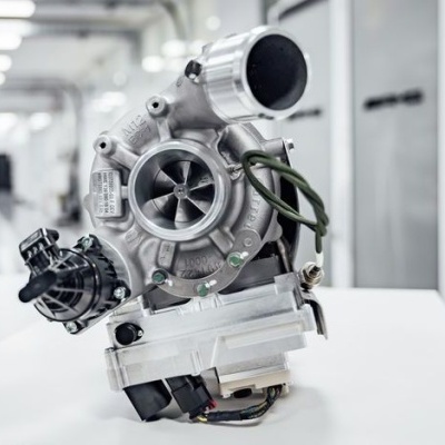 Turbocompressor metálico cinza com componentes a preto e cabo verde sobre mesa branca