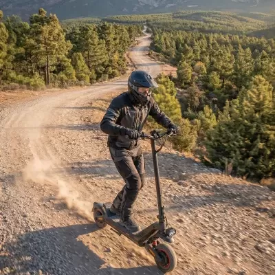Utilizador com equipamento preto num patinete elétrico negro em estrada de terra batida com árvores e montanhas ao fundo