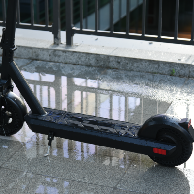 Patinete elétrico preto numa superfície molhada refletiva junto a uma grade preta