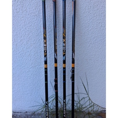 Quatro canas de pesca telescópicas KASHIMA TREX encostadas a uma parede branca com chão de cimento e plantas secas ao lado.