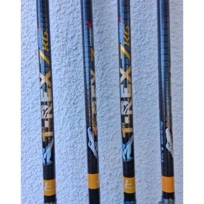 Quatro varas de pesca pretas com detalhes amarelos e texto TREX 7 KG junto a uma parede branca.