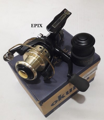 Carreto de pesca preto e dourado em caixa OKUMA com objeto preto ao lado