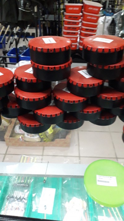 Recipientes redondos com tampa vermelha e corpo preto empilhados numa loja