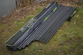 Kit de canas de pesca pretas com detalhes verdes num estojo ao lado de um lago sobre a relva