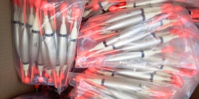 Boias de pesca prateadas com topos vermelhos e pretos embaladas em plástico dentro de caixa de papelão