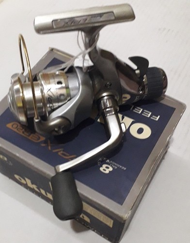 Carreto de pesca prateado e preto sobre caixa azul com texto