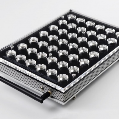 Aparelho retangular metálico com refletores circulares e cabo preto