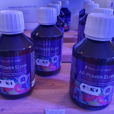 Garrafas pretas de AF Power Elixir com rótulos coloridos e tampas brancas num tampo de madeira