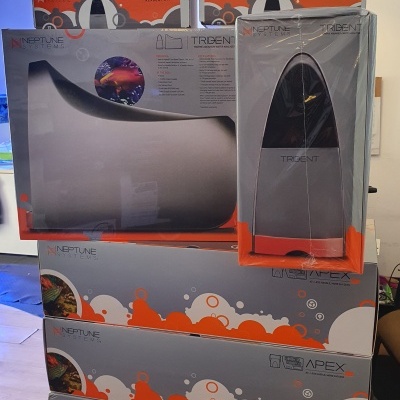 Caixas de produtos Neptune Systems cinzentas com detalhes laranja e texto Trident e Apex