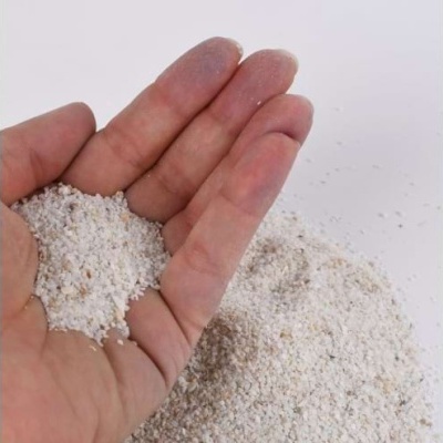 Mão segurando areia branca fina sobre fundo branco.