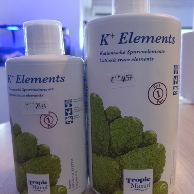 Duas garrafas brancas do produto K+ Elements com ilustração de algas verdes e texto em alemão e inglês.