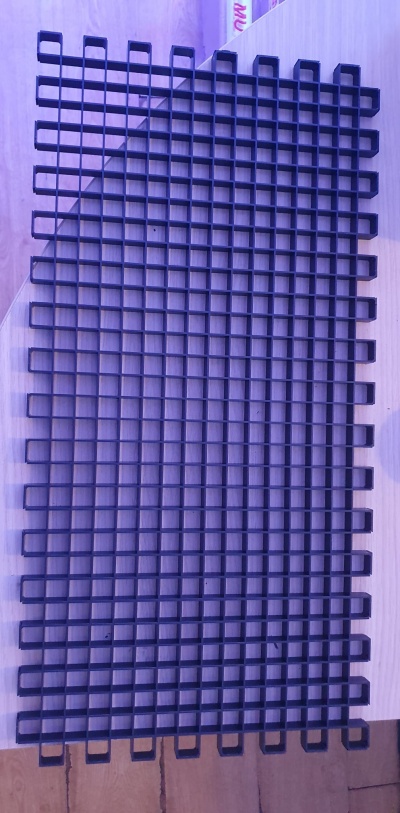 Grade metálica retangular preta com quadrados sobre madeira clara