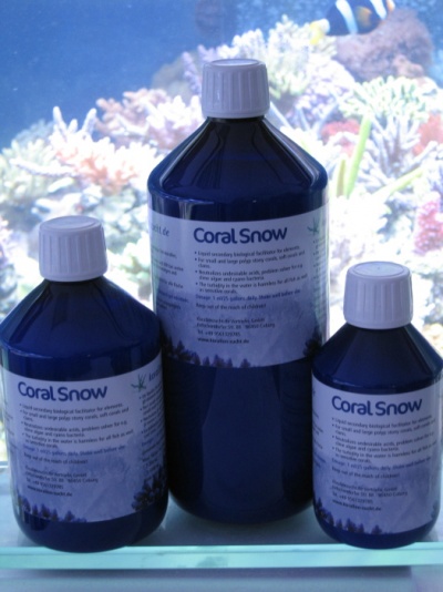 Três frascos azuis do produto Coral Snow em frente a aquário com corais