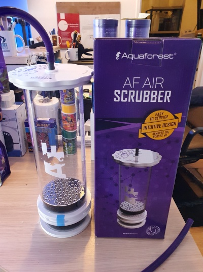 Dispositivo cylindrical transparente com base e topo brancos, tubo roxo conectado no topo, ao lado da caixa roxa da marca Aquaforest com texto AF AIR SCRUBBER