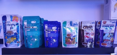 Embalagens variadas de snacks ou suplementos alimentares em prateleira, com textos MARINE A, CASE CUISINE e COMPLÉMENT DIÉTÉTIQUE