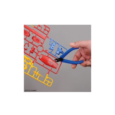 Mão usando alicate azul para cortar peça vermelha de plástico em moldura colorida.