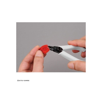 Mãos segurando uma ferramenta branca a cortar uma peça vermelha de plástico sobre fundo cinza.