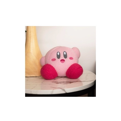 Pelúcia rosa do personagem Kirby com sapatos vermelhos sobre mesa branca com veios cinzentos ao lado de objeto de madeira