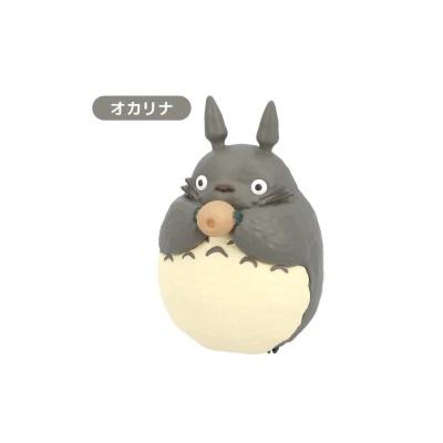 Figura Totoro cinzenta e creme a segurar um instrumento tipo ocarina com texto japonês.