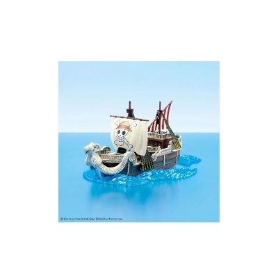 Miniatura de barco pirata com vela de crânio com chapéu, casco de madeira e figura de carneiro na proa sobre ondas azuis.