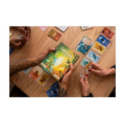 Jogo de cartas A Familiar Find com cartas coloridas e pessoas a jogar numa mesa de madeira clara