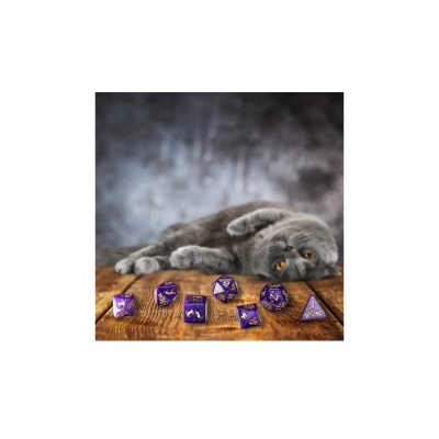 Dados roxos com números dourados sobre mesa de madeira e gato cinzento ao fundo