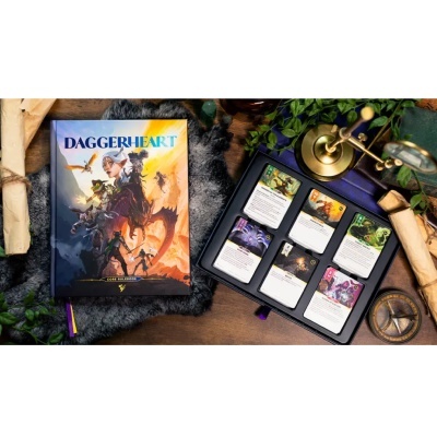 Livro DAGGERHEART com cartas de jogo e acessórios decorativos numa mesa de madeira