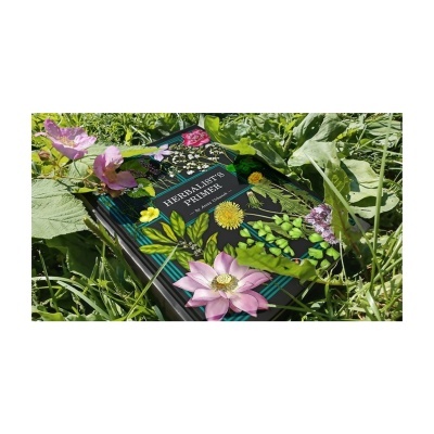 Livro HERBALISTS PRIMER com capa preta e plantas ao redor