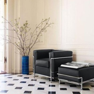cadeira e otoman pretos com vaso azul e chão geométrico