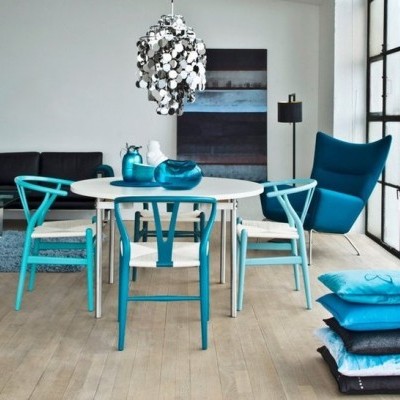 Sala de jantar com mesa redonda branca e cadeiras azuis, cadeira azul escura, sofá preto, almofadas azuis e lustre prateado