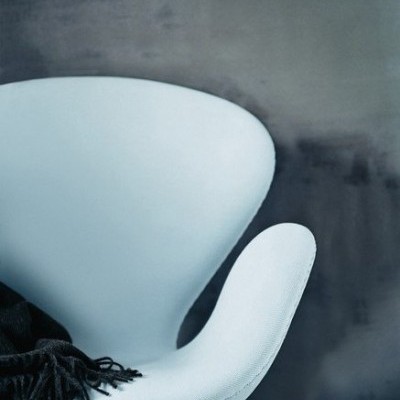 Cadeira branca moderna com manta preta sobre o braço contra parede escura