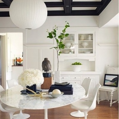 Mesa de jantar redonda em mármore com cadeiras brancas modernas num espaço decorado com flores, esculturas e fruteira com limões