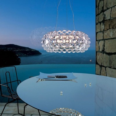 Luminária suspensa redonda de esferas de vidro transparente sobre mesa azul claro com vista para o mar