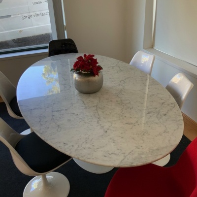 Mesa oval de mármore branco com cadeiras coloridas e vaso com flores no centro