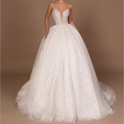 Vestido de noiva branco volumoso com corpete transparente e saia brilhante num fundo castanho.