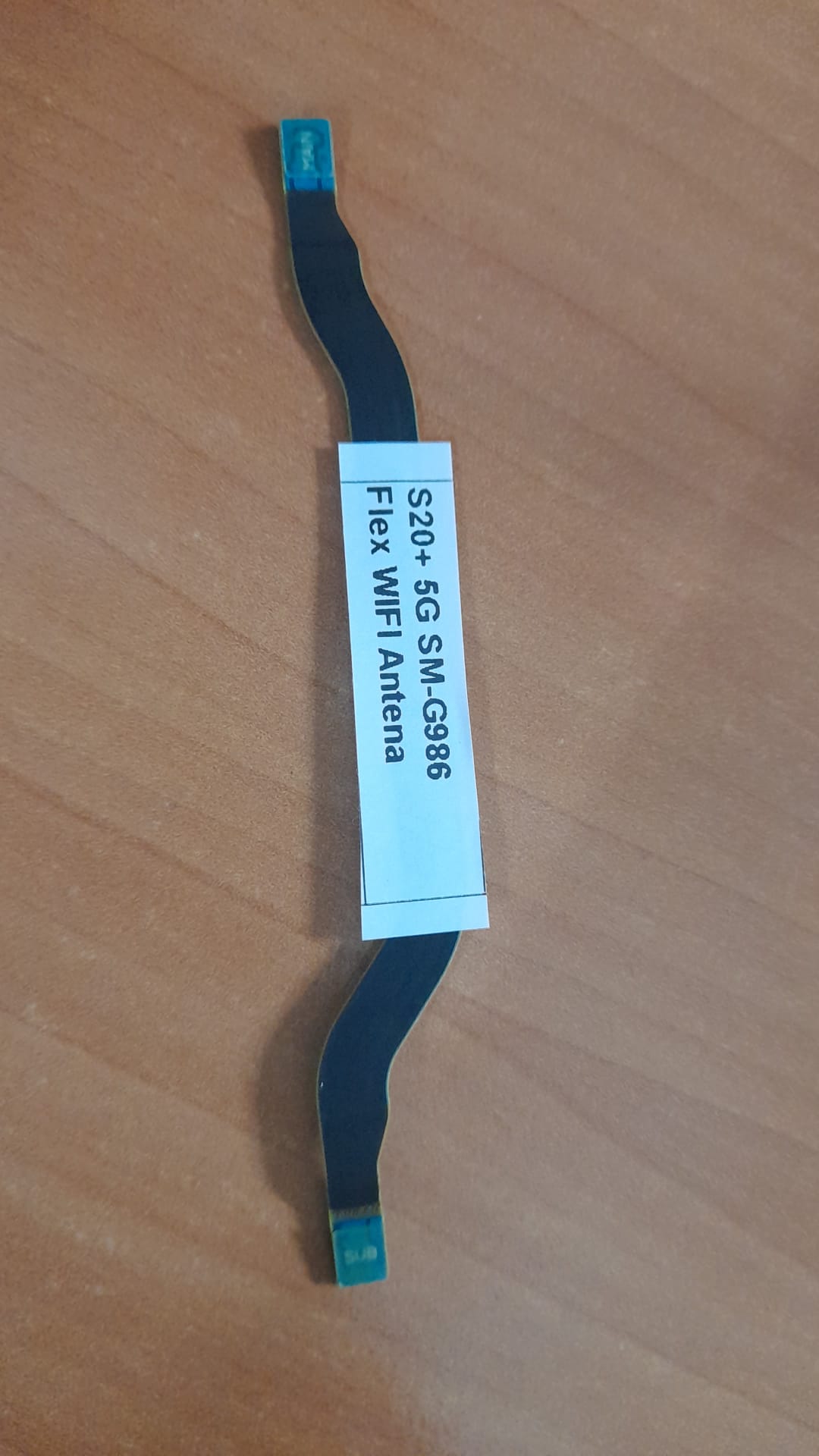 Cabo Flex de Antena Wi-Fi Samsung Galaxy S20+ (SM-G986) – Original OEM – Testado Cabo flexível preto com etiqueta branca para antena WiFi sobre madeira clara